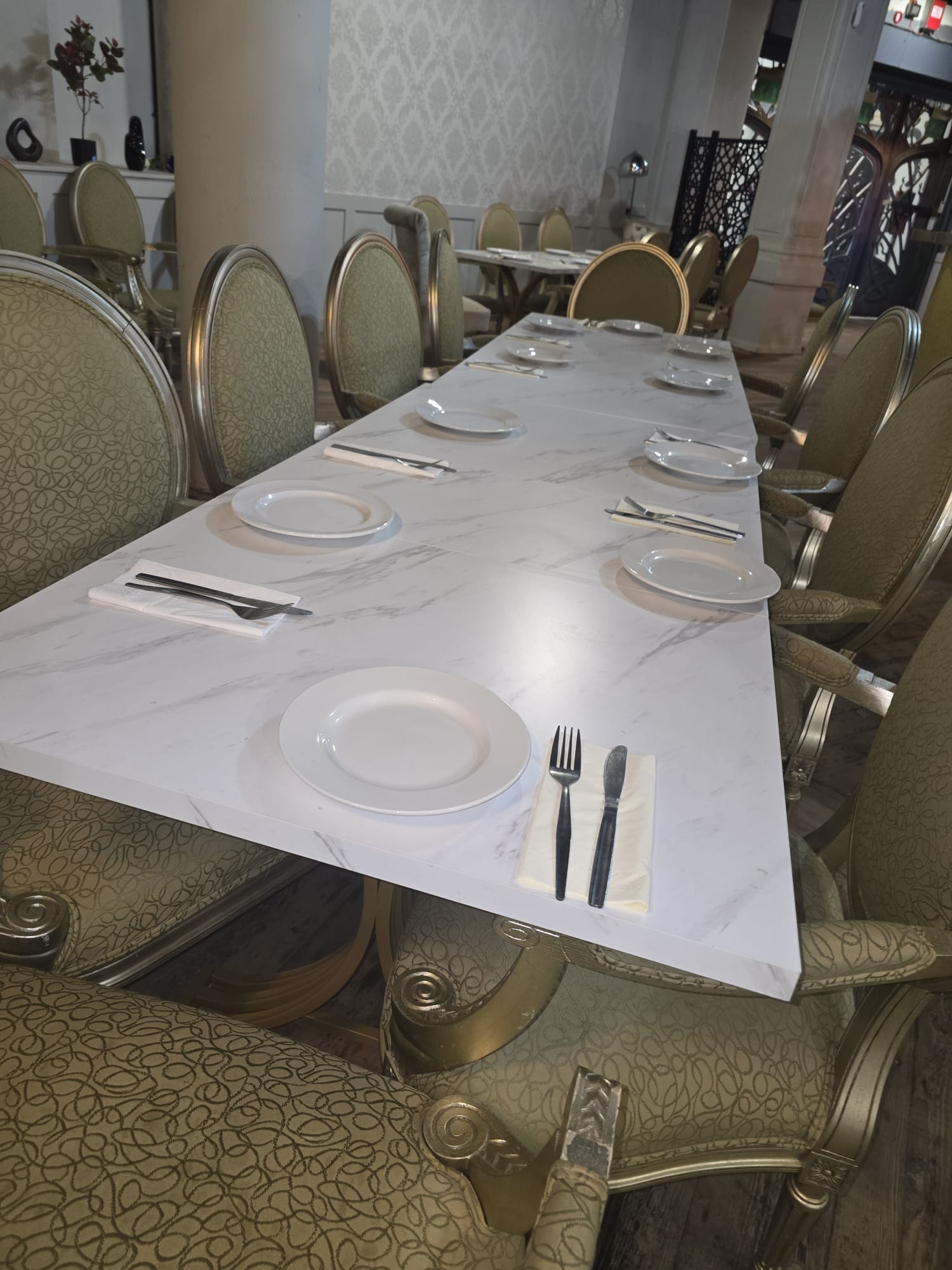 Long marble-top dining table with white china place settings and gold oval-back chairs at Opulent @ 35 Liverpool