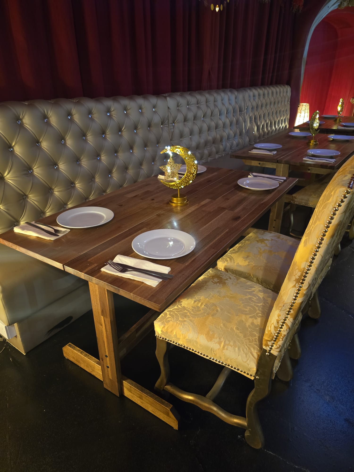 Close-up of Fozia's tufted banquette dining at Opulent @ 35 Liverpool — wood tables, white china and gold crescent centrepiece