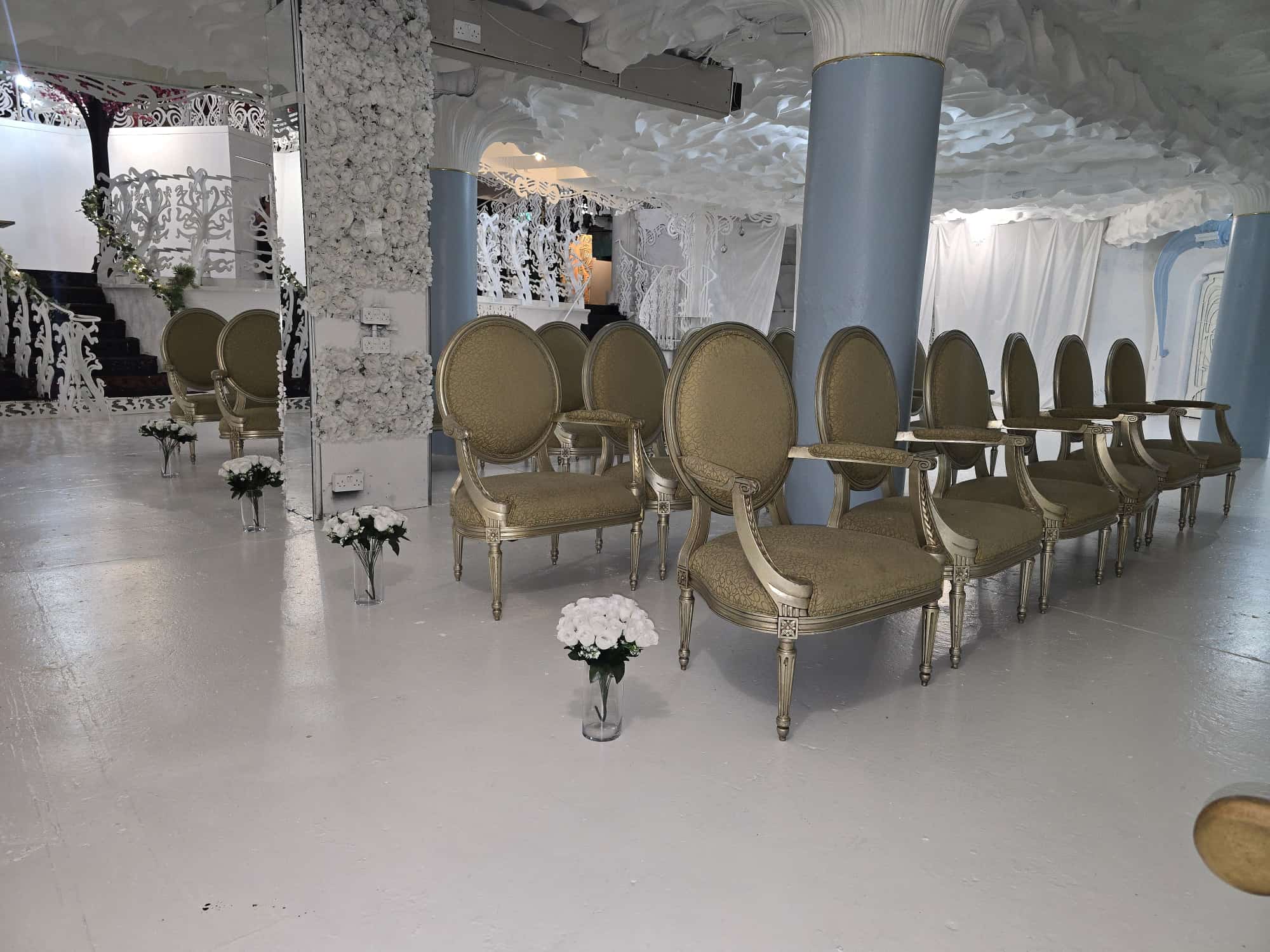 Rows of gold damask oval-back chairs arranged for a Nikah ceremony beside a mirrored column and white floral wall inside Opulent @ 35 Liverpool