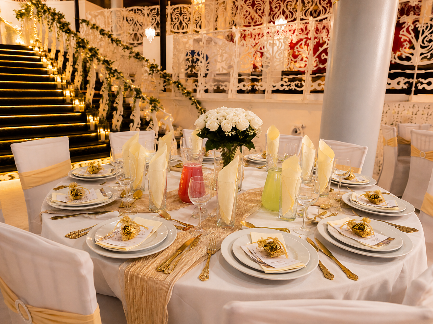 Round wedding table with cream napkin fans, gold cutlery and pink and green mocktails beside the candlelit Art Nouveau staircase at Opulent @ 35 Liverpool